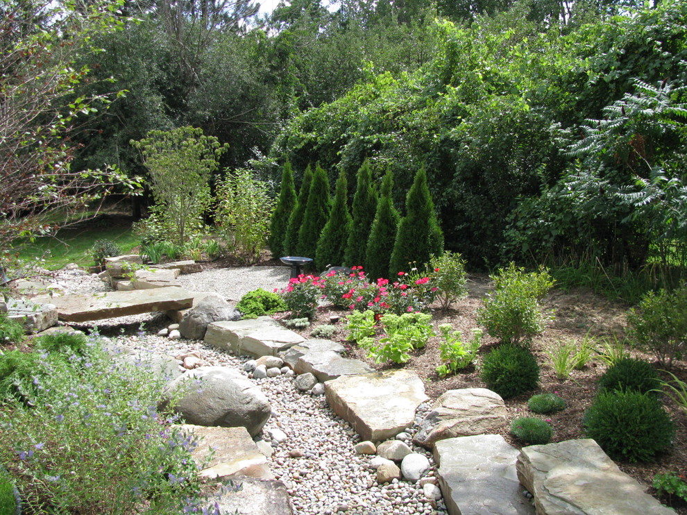Diseño de jardín de secano rural pequeño en verano en patio trasero con exposición total al sol, adoquines de piedra natural y muro de contención
