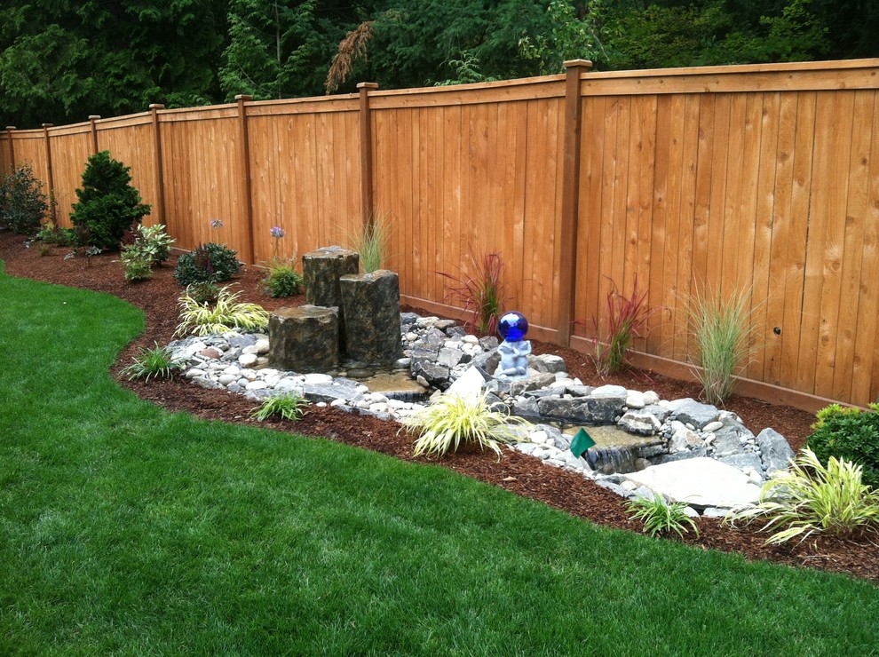 This is an example of a medium sized world-inspired back full sun garden in Seattle with a water feature and mulch.