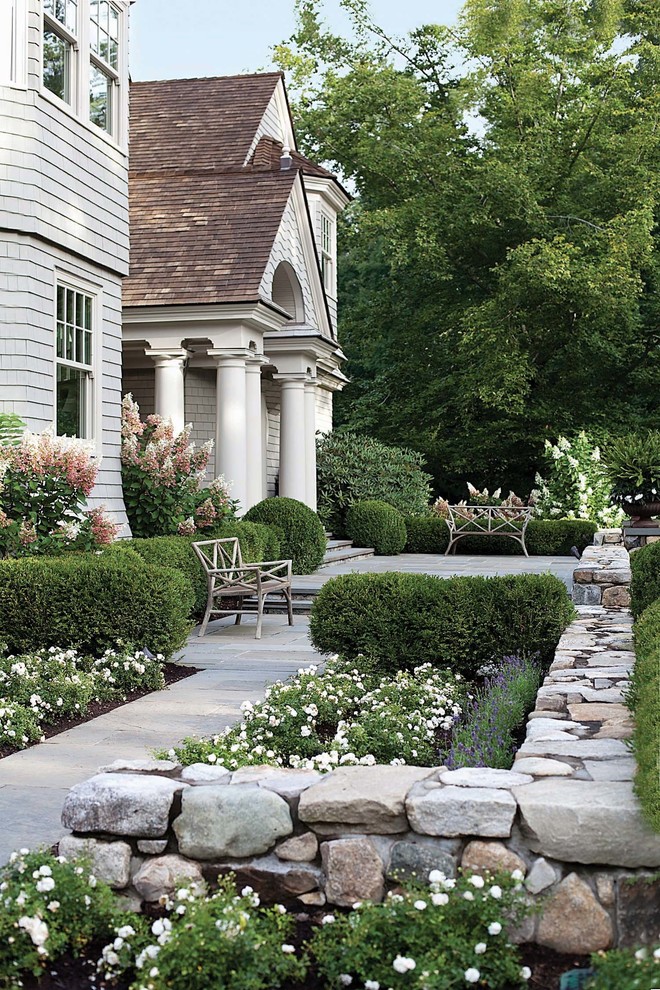Modelo de jardín clásico de tamaño medio en verano en patio delantero con adoquines de piedra natural, exposición total al sol, jardín francés y parterre de flores