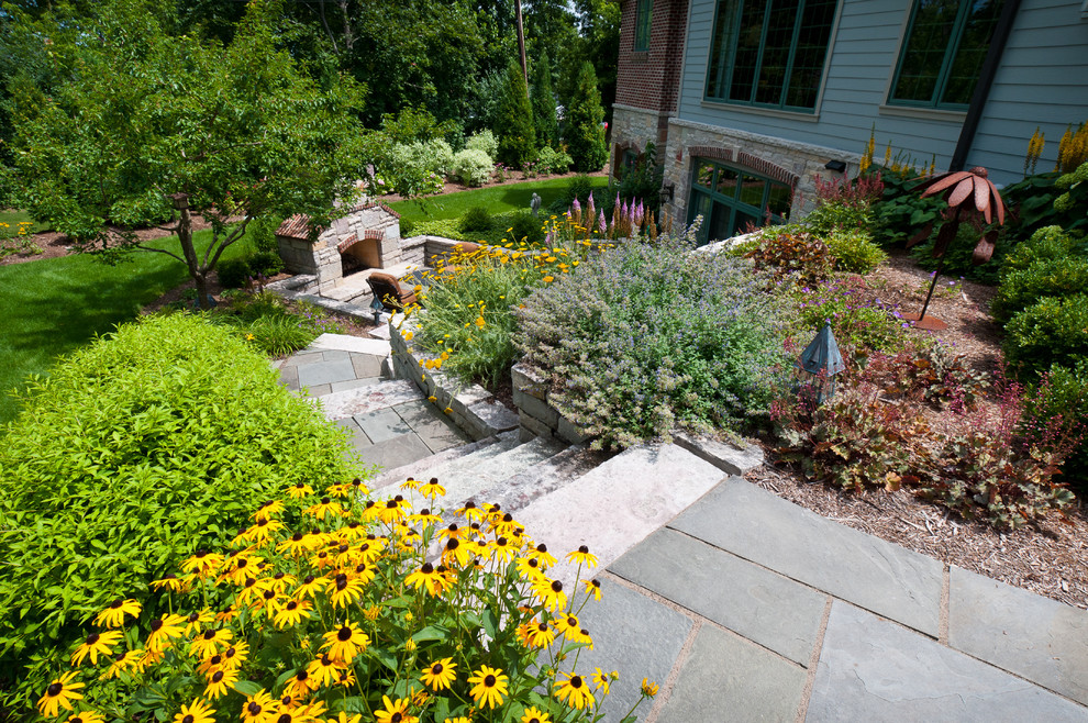 This is an example of a mid-sized traditional full sun backyard stone retaining wall landscape in Milwaukee for summer.