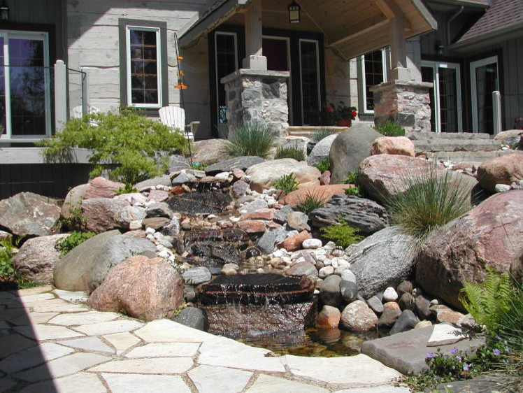 Modelo de jardín rural de tamaño medio en patio delantero con exposición total al sol, adoquines de piedra natural y muro de contención