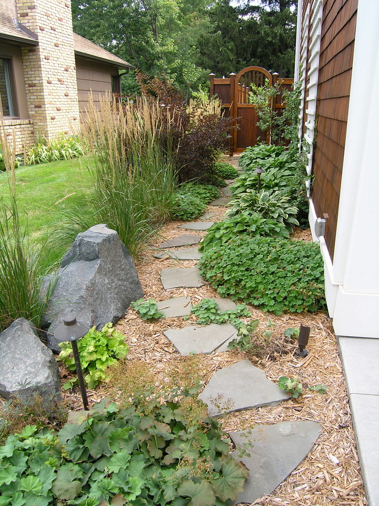 Réalisation d'un aménagement d'entrée ou allée de jardin latéral tradition avec des pavés en pierre naturelle.