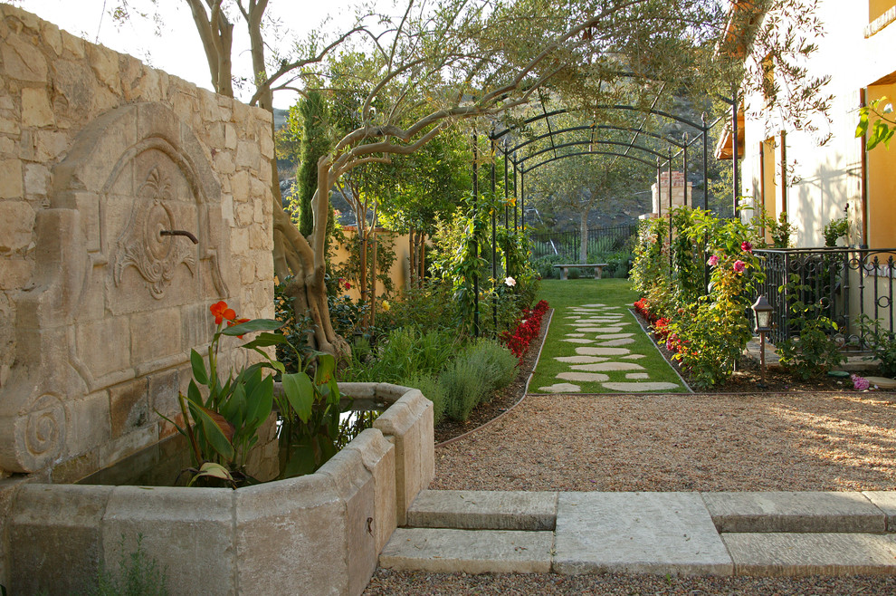 Foto di un giardino formale mediterraneo esposto in pieno sole dietro casa in primavera con pavimentazioni in pietra naturale