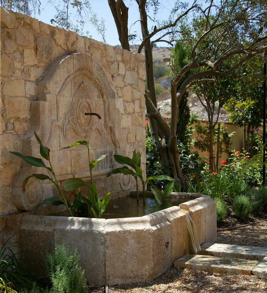 Exempel på en stor medelhavsstil trädgård i full sol, med en fontän och naturstensplattor