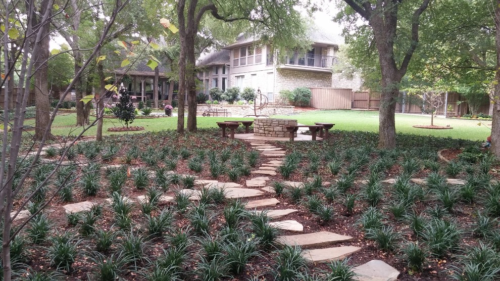 This is an example of an expansive back fully shaded garden for summer in Dallas with a fire feature and natural stone paving.