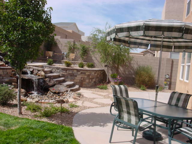 Cette image montre un grand jardin arrière sud-ouest américain l'été avec un bassin, une exposition ensoleillée et des pavés en brique.