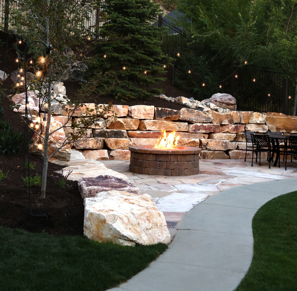 Klassischer Garten hinter dem Haus mit Feuerstelle, Natursteinplatten und Metallzaun in Salt Lake City