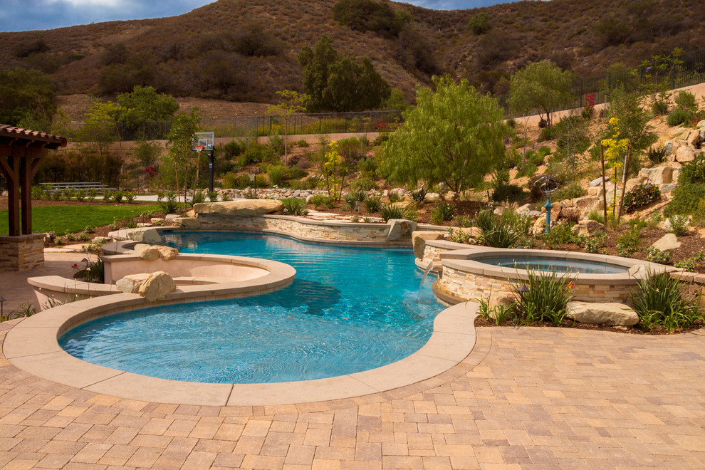 Diseño de piscina actual de tamaño medio en patio trasero con adoquines de hormigón
