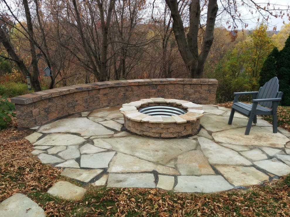 This is an example of a large rustic back patio in Minneapolis with a fire feature and natural stone paving.