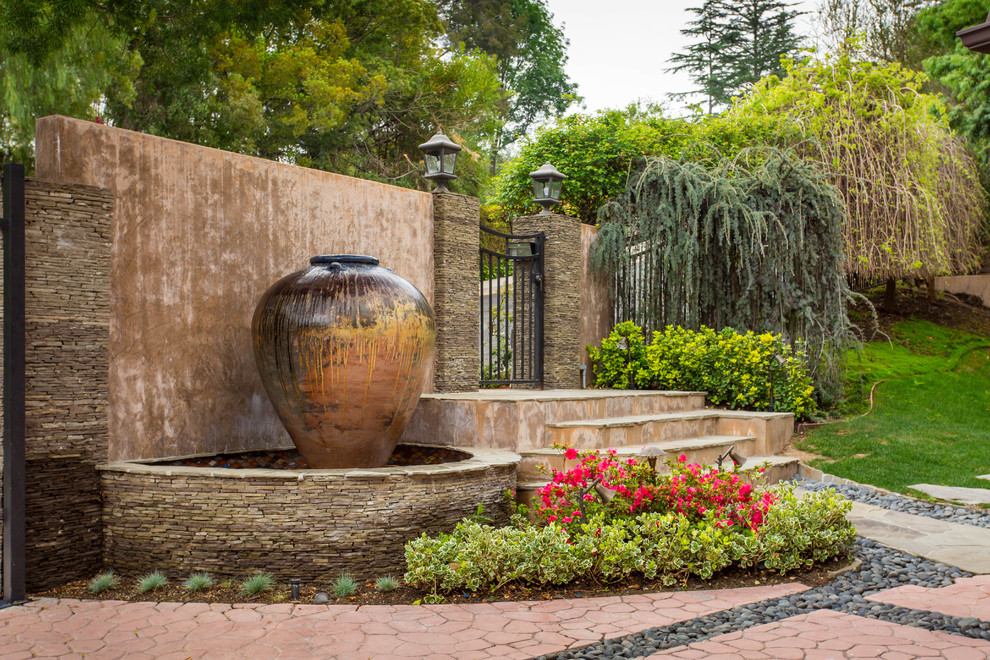 Large mediterranean front driveway partial sun garden in Los Angeles with a water feature and concrete paving.