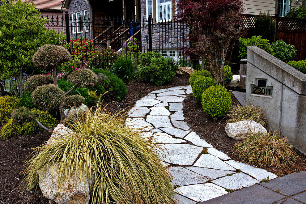 Small world-inspired front full sun garden in Other with natural stone paving and a flowerbed.