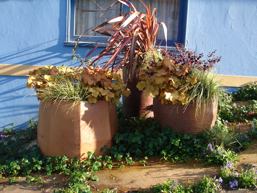 Bild på en liten medelhavsstil trädgård i skuggan framför huset, med utekrukor och naturstensplattor