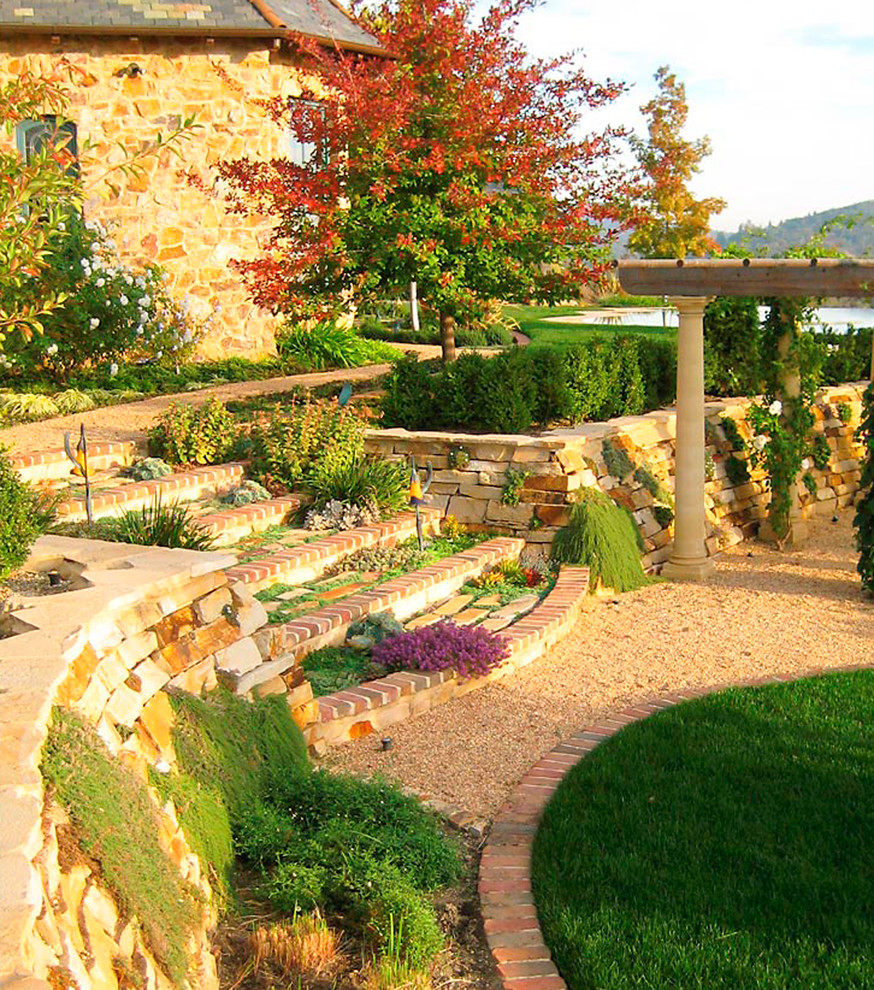 Esempio di un ampio giardino mediterraneo esposto in pieno sole in autunno con un muro di contenimento, un pendio, una collina o una riva e pavimentazioni in pietra naturale