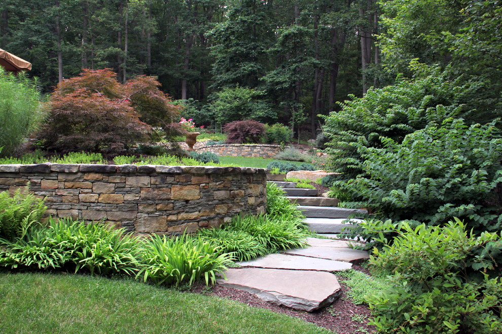 This is an example of a large classic back full sun garden in DC Metro with a retaining wall and natural stone paving.