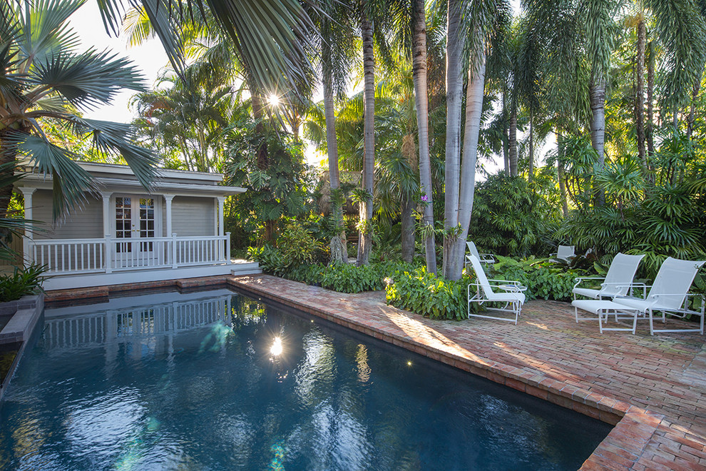 Bild på en mellanstor tropisk trädgård längs med huset, med marksten i tegel