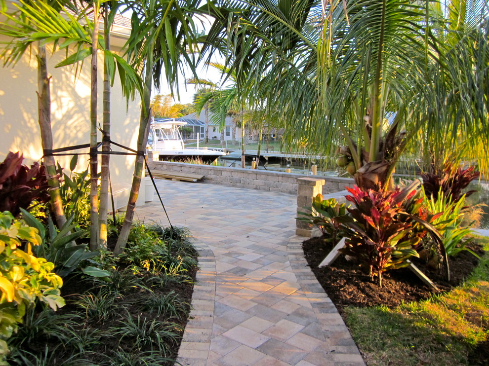 Diseño de jardín exótico grande en patio trasero con muro de contención, jardín francés, exposición parcial al sol y adoquines de ladrillo