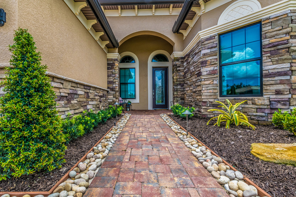 Photo of a mid-sized tropical front yard stone driveway in Miami.