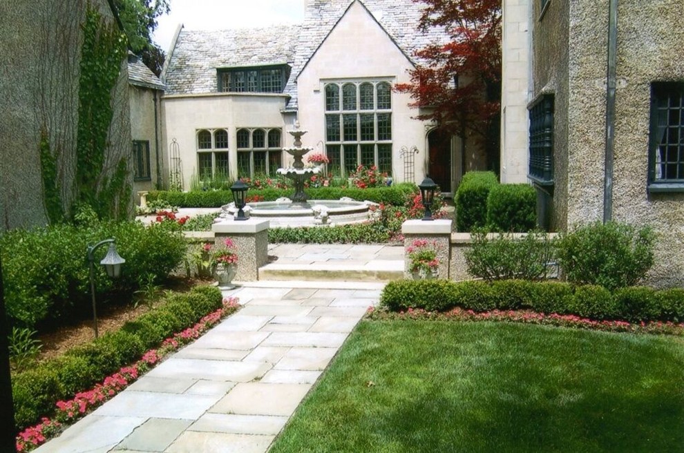 Imagen de jardín clásico de tamaño medio en primavera en patio trasero con jardín francés, fuente, exposición total al sol y adoquines de piedra natural