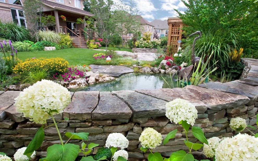 Foto di un grande laghetto da giardino tradizionale esposto in pieno sole dietro casa in primavera con pavimentazioni in pietra naturale