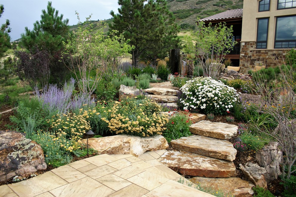 Стильный дизайн: большой солнечный, летний засухоустойчивый сад на склоне в средиземноморском стиле с садовой дорожкой или калиткой, хорошей освещенностью, покрытием из каменной брусчатки и с металлическим забором - последний тренд