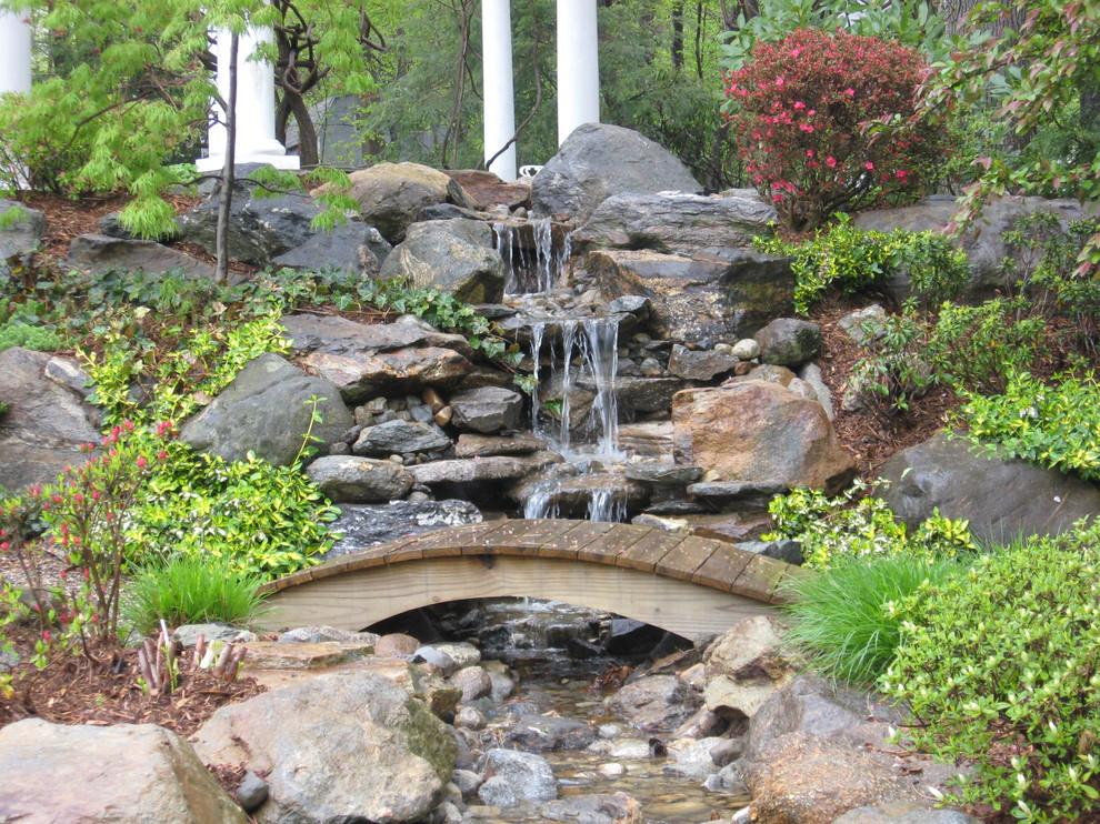 Réalisation d'un jardin arrière tradition avec des pavés en pierre naturelle et une cascade.
