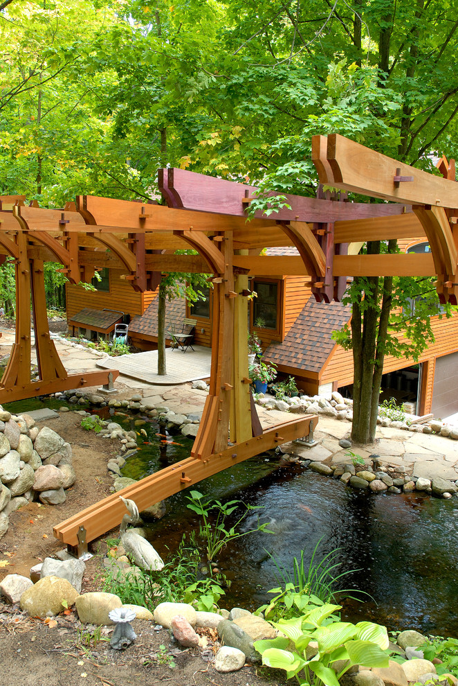 This is an example of an eclectic backyard pond in Other with a pergola.