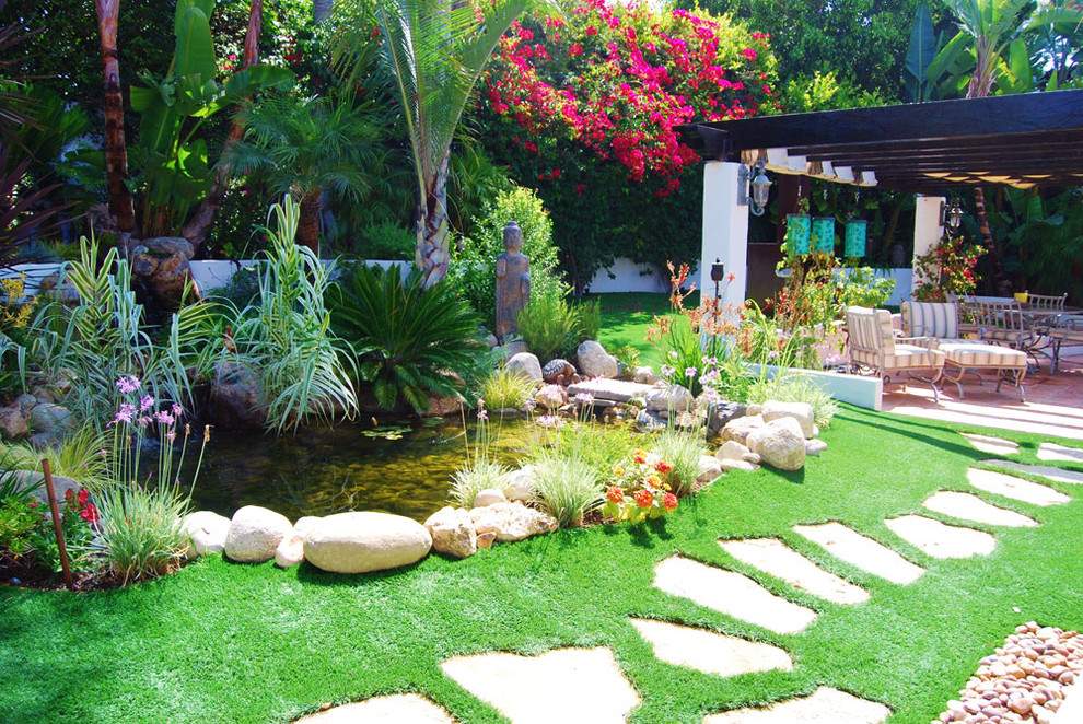 Imagen de jardín tropical de tamaño medio en patio trasero con fuente, exposición parcial al sol y adoquines de piedra natural