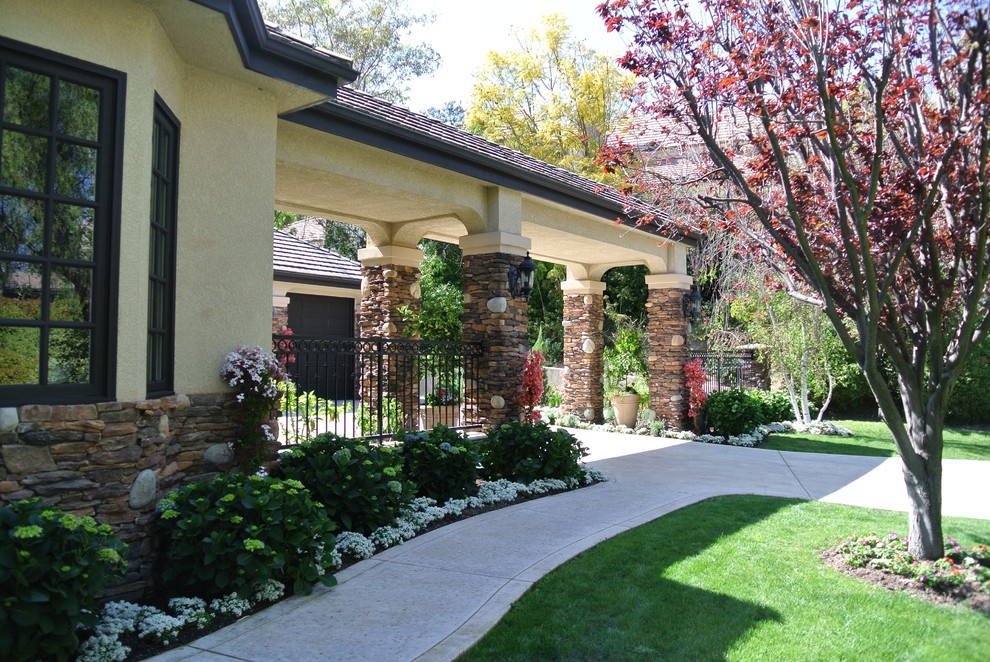 На фото: весенний регулярный сад среднего размера на переднем дворе в средиземноморском стиле с клумбами, полуденной тенью, мощением тротуарной плиткой и с металлическим забором