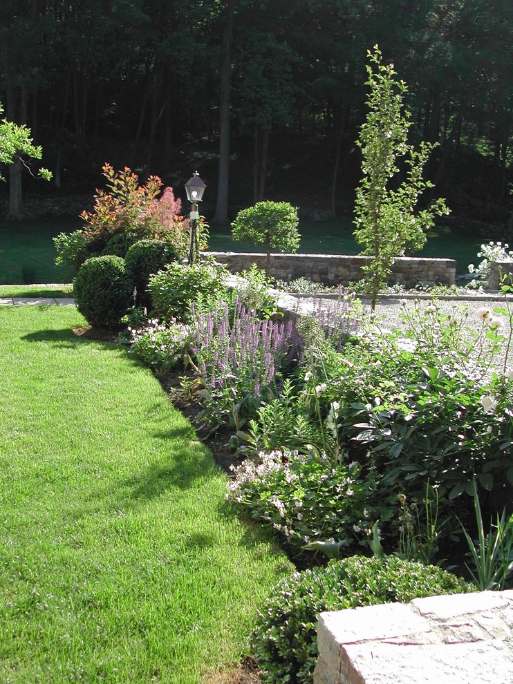 Esempio di un giardino formale tradizionale esposto a mezz'ombra di medie dimensioni e dietro casa in primavera con un muro di contenimento e ghiaia