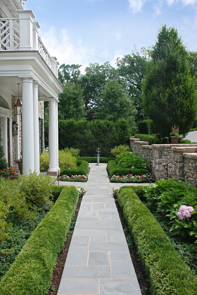 Réalisation d'un aménagement d'entrée ou allée de jardin avant tradition l'été avec une exposition ensoleillée et des pavés en pierre naturelle.
