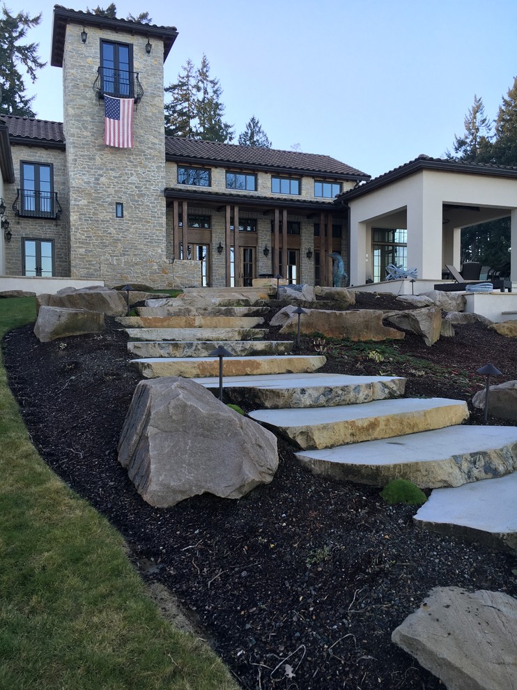 Large coastal sloped full sun garden for summer in Seattle with natural stone paving.