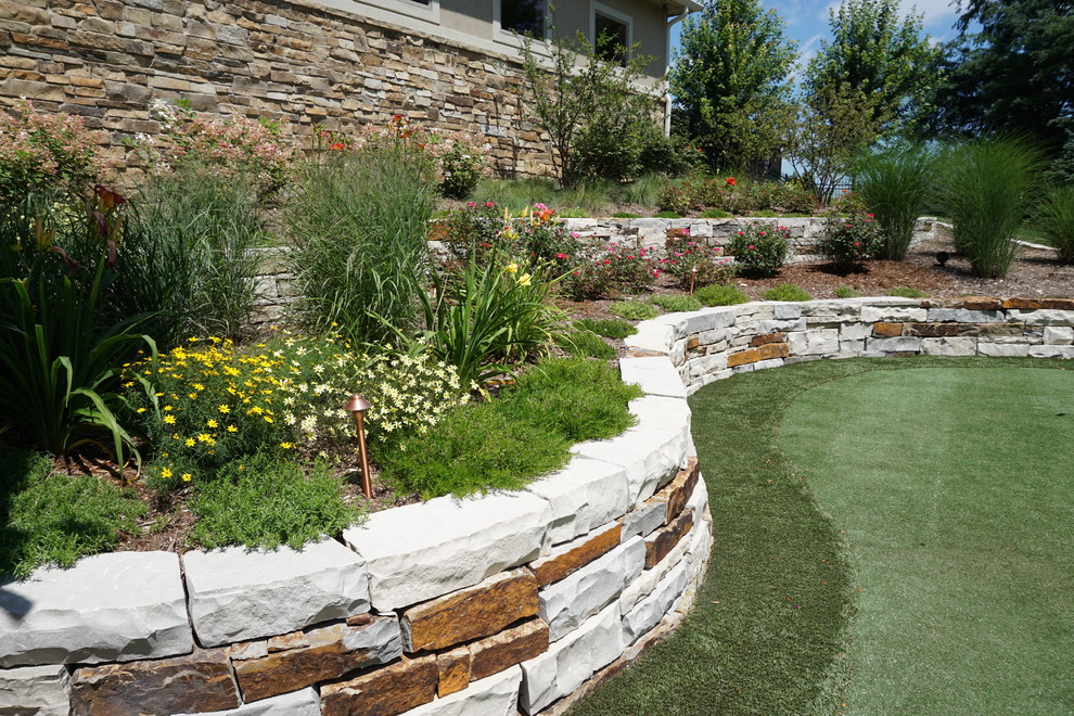 Immagine di un grande giardino tradizionale esposto in pieno sole dietro casa con un muro di contenimento e pavimentazioni in pietra naturale