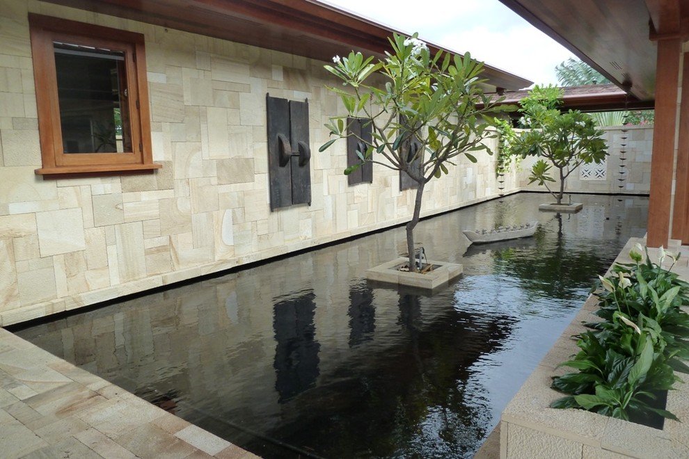 Foto di un grande laghetto da giardino tropicale esposto a mezz'ombra dietro casa con pavimentazioni in pietra naturale