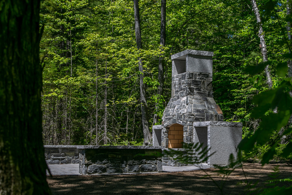 Réalisation d'un grand xéropaysage arrière tradition l'été avec une cheminée, une exposition partiellement ombragée et des pavés en béton.