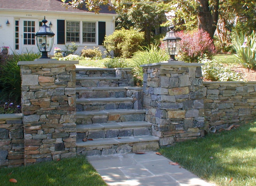 Immagine di un giardino esposto in pieno sole davanti casa con un muro di contenimento e pavimentazioni in pietra naturale