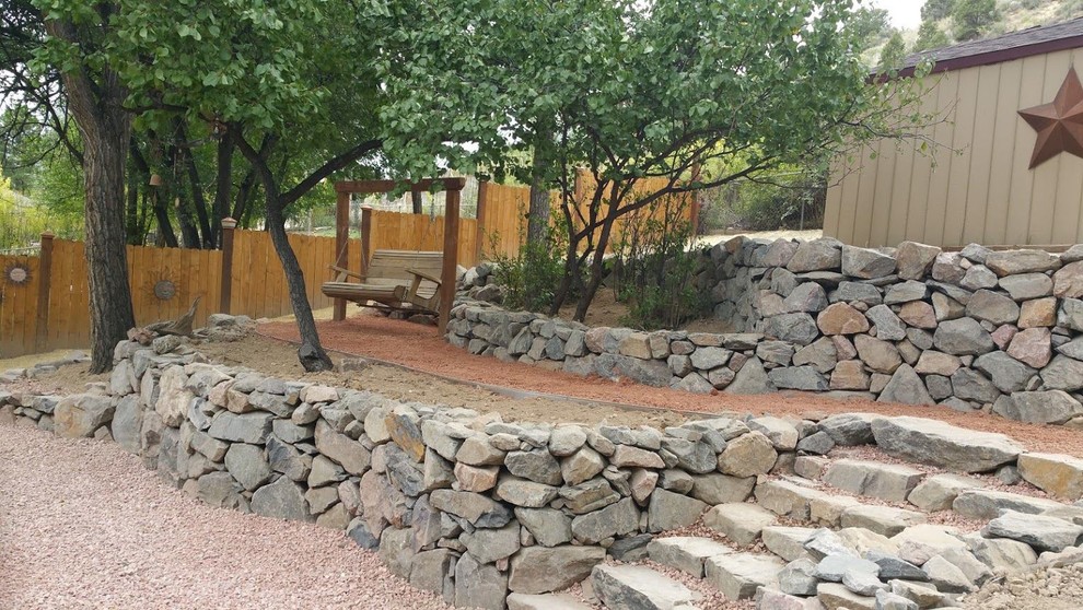 This is an example of a large rustic back xeriscape full sun garden in Denver with a retaining wall and gravel.