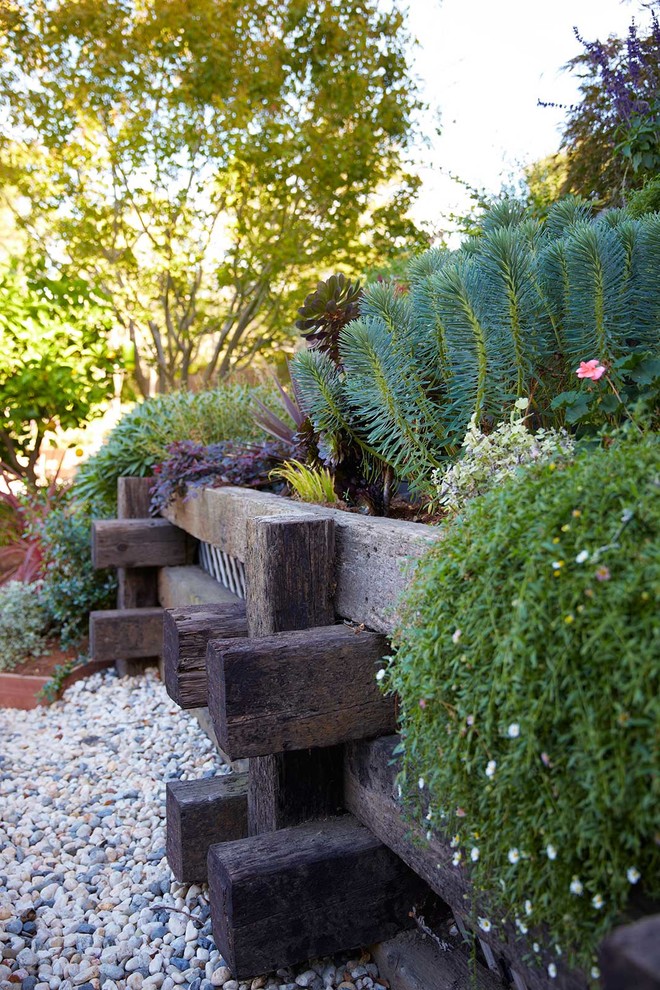 Inspiration för stora moderna trädgårdar i skuggan i slänt på sommaren, med en stödmur och grus