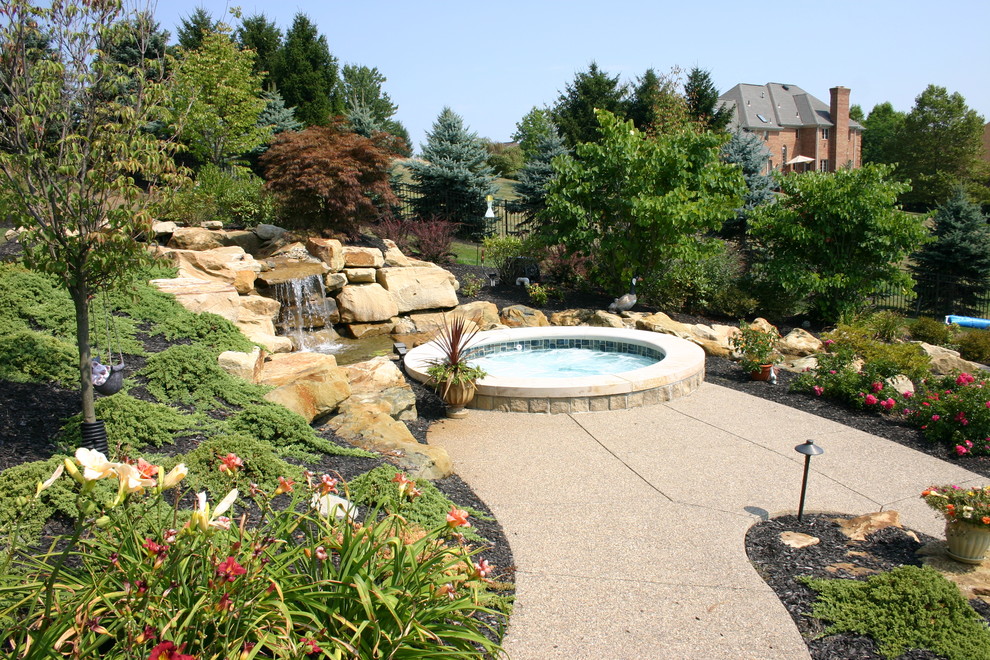 Imagen de jardín actual grande en verano en patio trasero con exposición total al sol y adoquines de hormigón