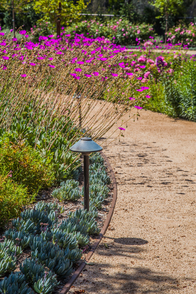 На фото: солнечный, летний засухоустойчивый сад на склоне в средиземноморском стиле с подпорной стенкой, хорошей освещенностью и покрытием из гравия с