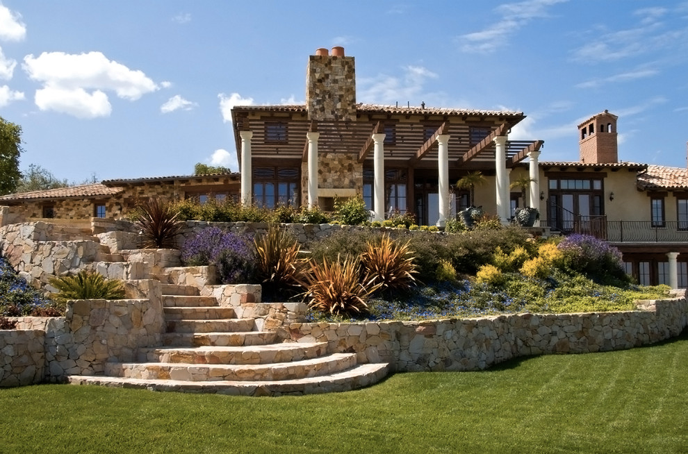 Idee per un grande giardino formale mediterraneo esposto in pieno sole dietro casa in estate con un muro di contenimento e pavimentazioni in pietra naturale