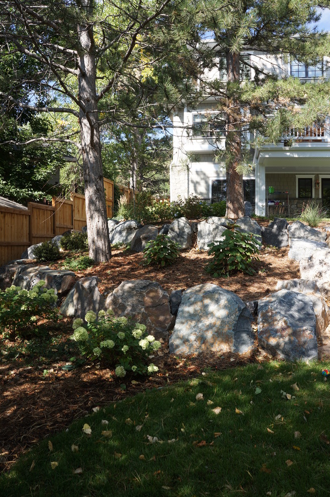 Aménagement d'un grand jardin arrière classique l'été avec un mur de soutènement, une exposition partiellement ombragée et des pavés en pierre naturelle.