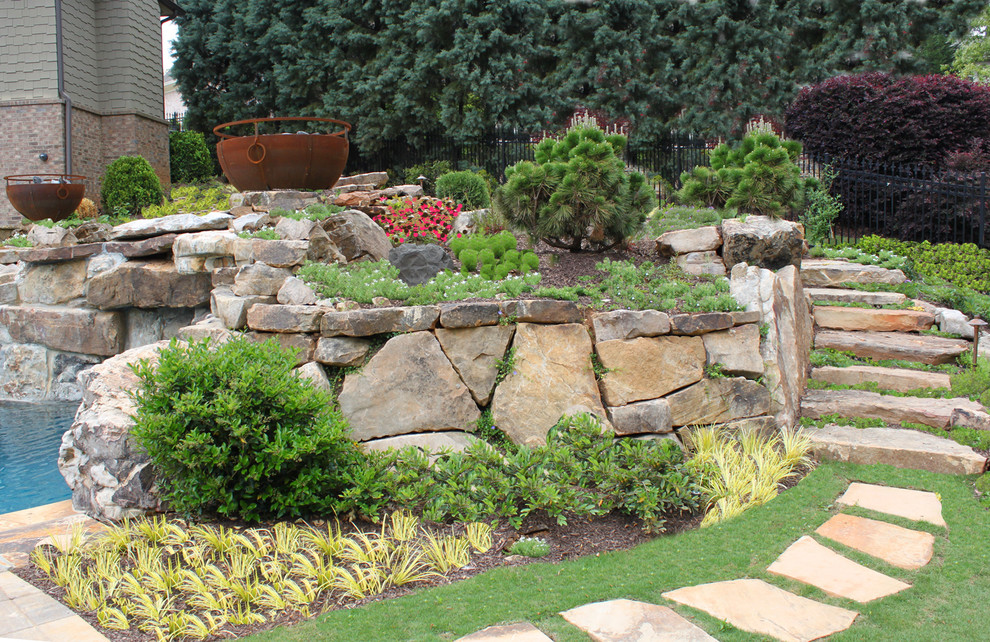 Idée de décoration pour un grand jardin arrière tradition avec un mur de soutènement, une exposition ensoleillée et des pavés en pierre naturelle.