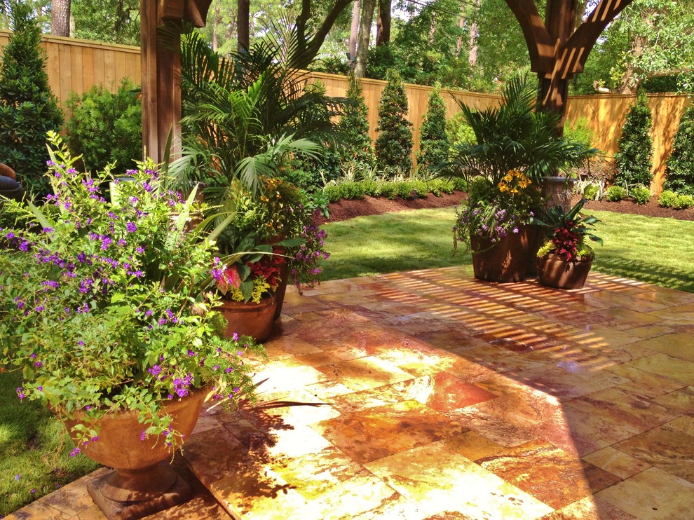 На фото: большой весенний регулярный сад на заднем дворе в средиземноморском стиле с растениями в контейнерах, полуденной тенью и покрытием из каменной брусчатки с