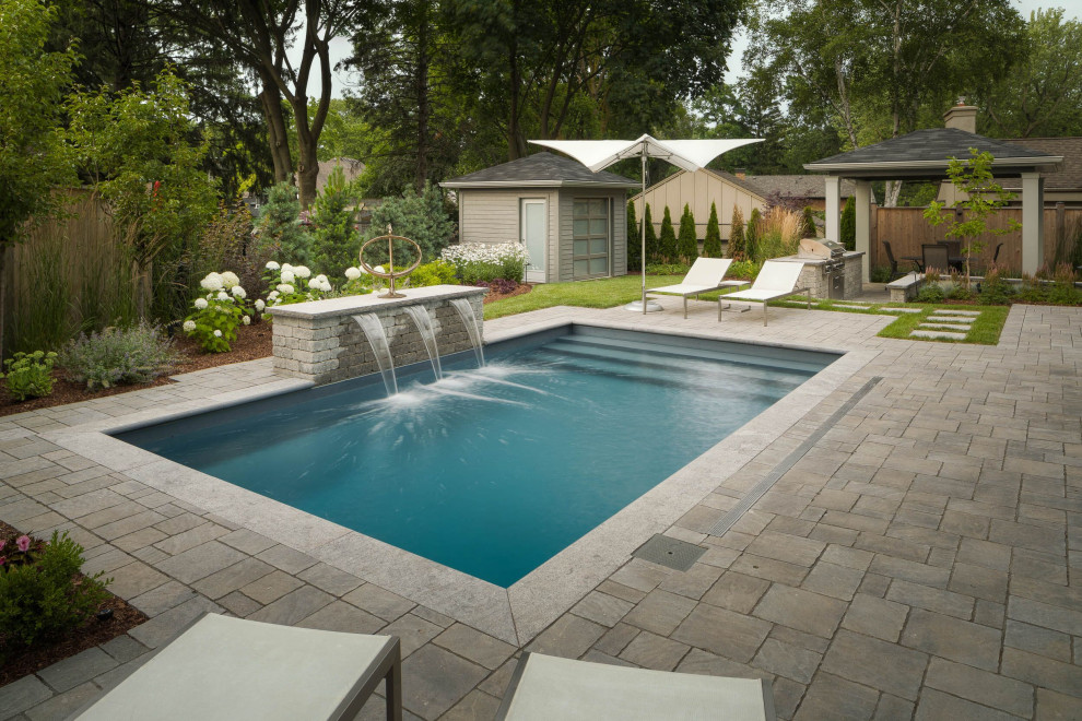 This is an example of a large contemporary back swimming pool in Toronto with natural stone paving.