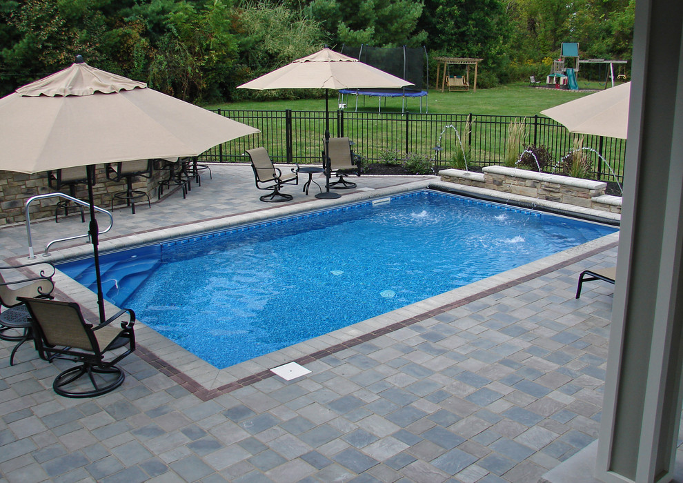 Ejemplo de piscina clásica de tamaño medio en patio trasero con adoquines de hormigón