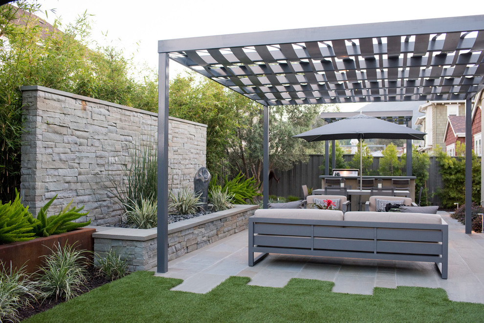Inspiration för mellanstora moderna bakgårdar i delvis sol, med en stödmur och naturstensplattor