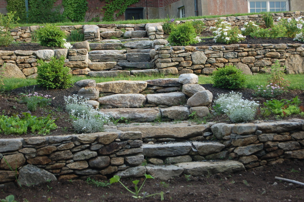 Imagen de jardín tradicional de tamaño medio en verano en patio trasero con jardín francés, muro de contención, exposición total al sol y adoquines de piedra natural