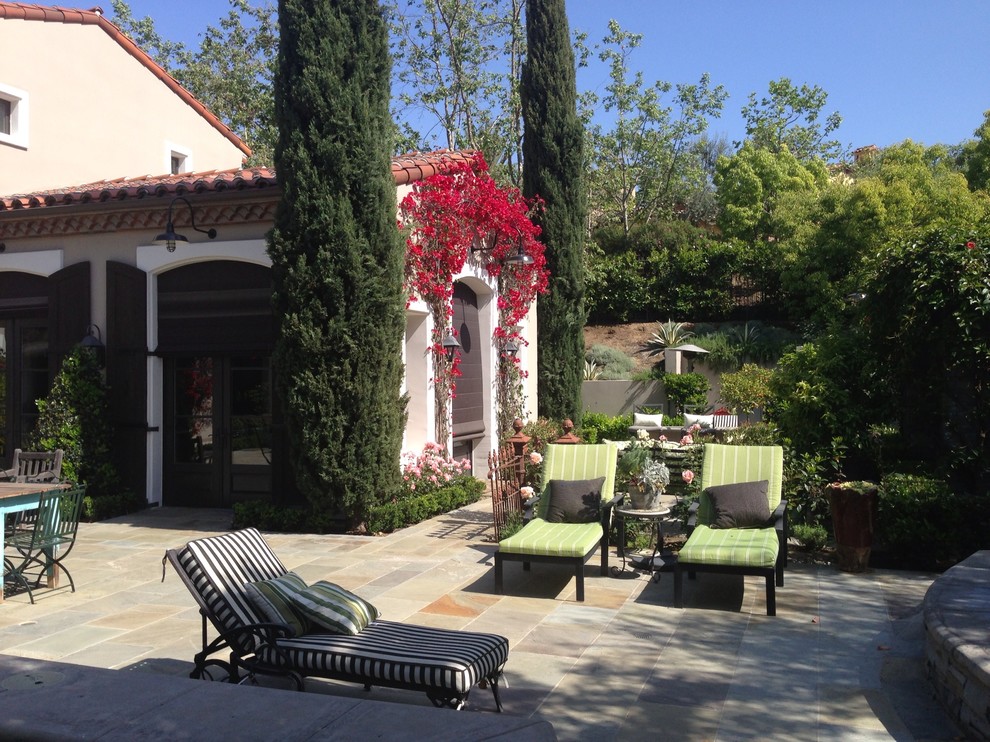 Großer Mediterraner Patio hinter dem Haus mit Wasserspiel und Natursteinplatten in Los Angeles
