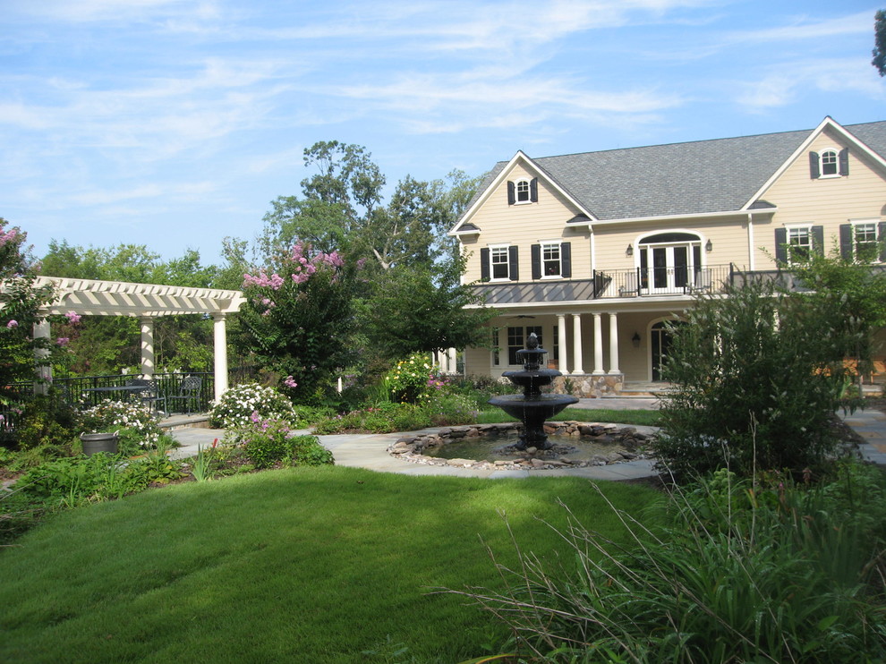 Exempel på en mycket stor klassisk formell trädgård i full sol framför huset på våren, med en fontän och naturstensplattor