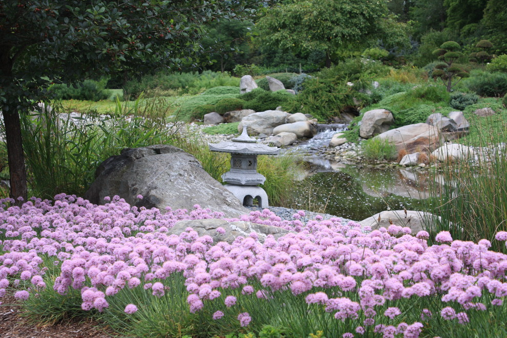 Réalisation d'un grand jardin arrière tradition avec un point d'eau et des pavés en pierre naturelle.